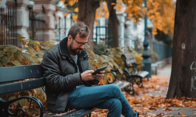 En man sitter på en parkbänk och lär sig med en ryska avancerad språkkurs